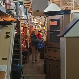 Binnenaanzicht van kringloopwinkel met stellingen, huisaccessoires en enkele bezoekers