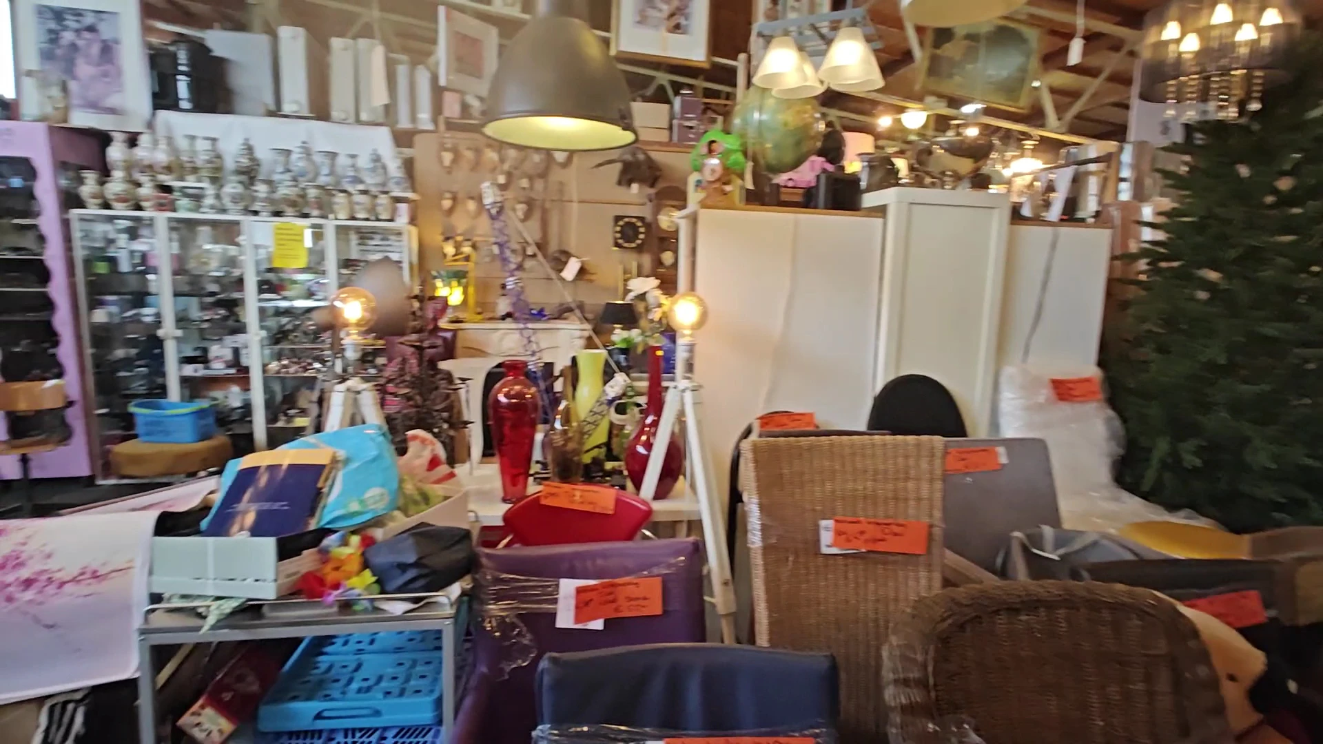 Binnenaanzicht van kringloopwinkel met stellingen, lampen, tassen en diverse tweedehandsartikelen