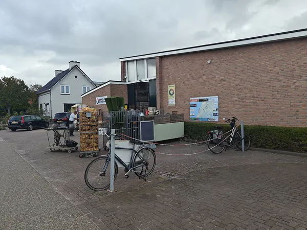 Voorkant van kringloopwinkel met bakstenen gevel, ingang en fietsen geparkeerd ervoor