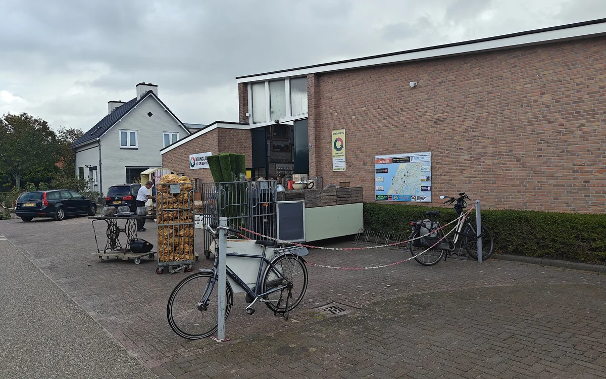Voorkant van kringloopwinkel met bakstenen gevel, ingang en fietsen geparkeerd ervoor