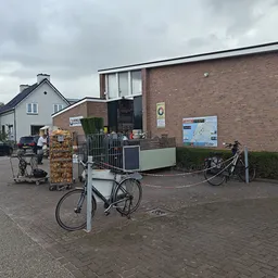 Voorkant van kringloopwinkel met bakstenen gevel, ingang en fietsen geparkeerd ervoor