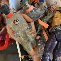 Diverse tweedehands speelgoed en plastic artikelen in plastic verpakking op een stapel