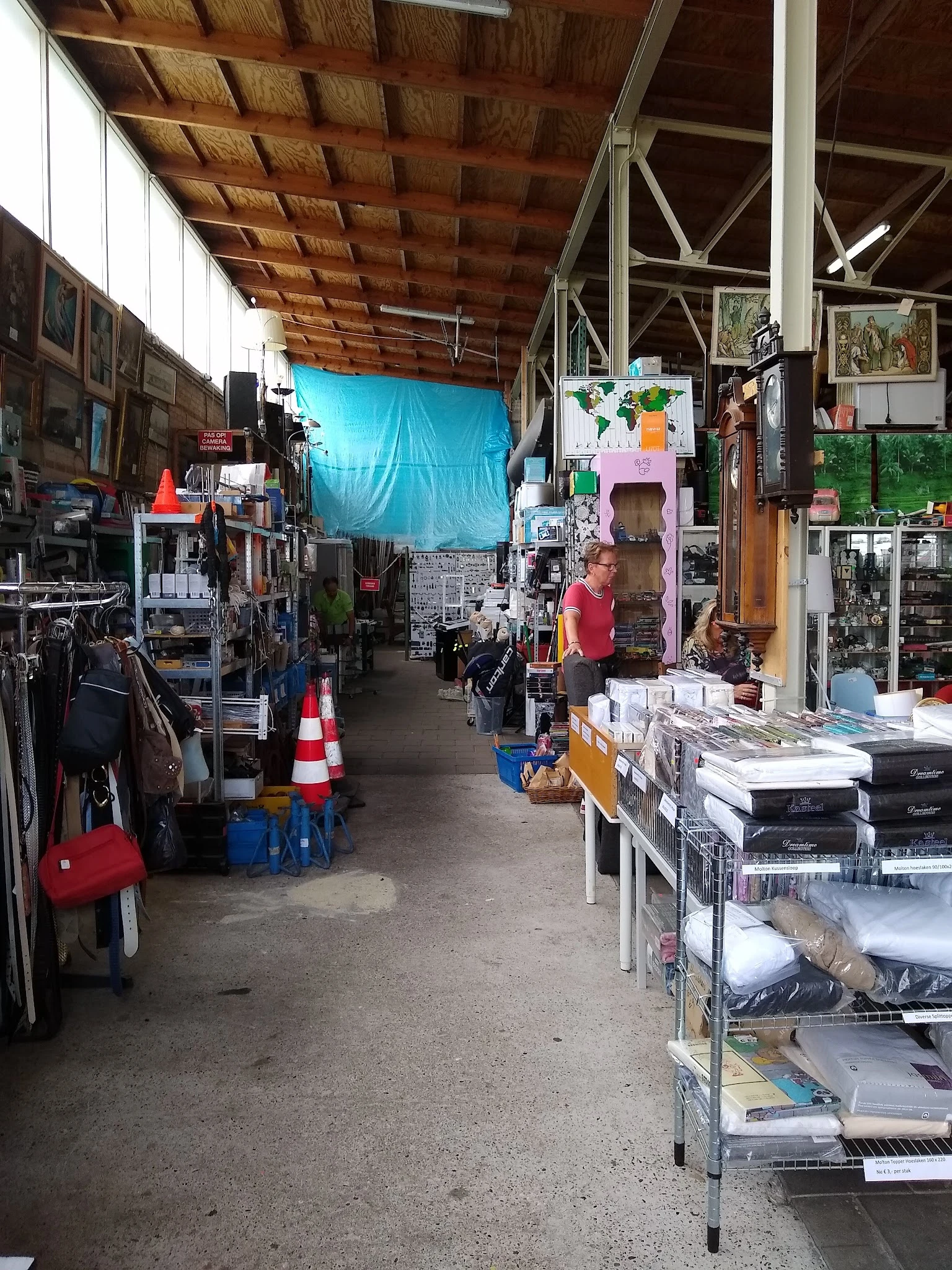 Binnenaanzicht van kringloopwinkel met stellingen, tafels vol spullen, kleding en diverse tweedehandsartikelen