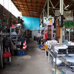 Binnenaanzicht van kringloopwinkel met stellingen, tafels vol spullen, kleding en diverse tweedehandsartikelen
