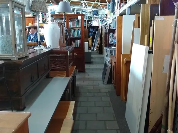 Binnenaanzicht van kringloopwinkel met schappen, boeken, meubels en diverse tweedehands artikelen langs de wanden
