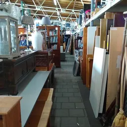 Binnenaanzicht van kringloopwinkel met schappen, boeken, meubels en diverse tweedehands artikelen langs de wanden