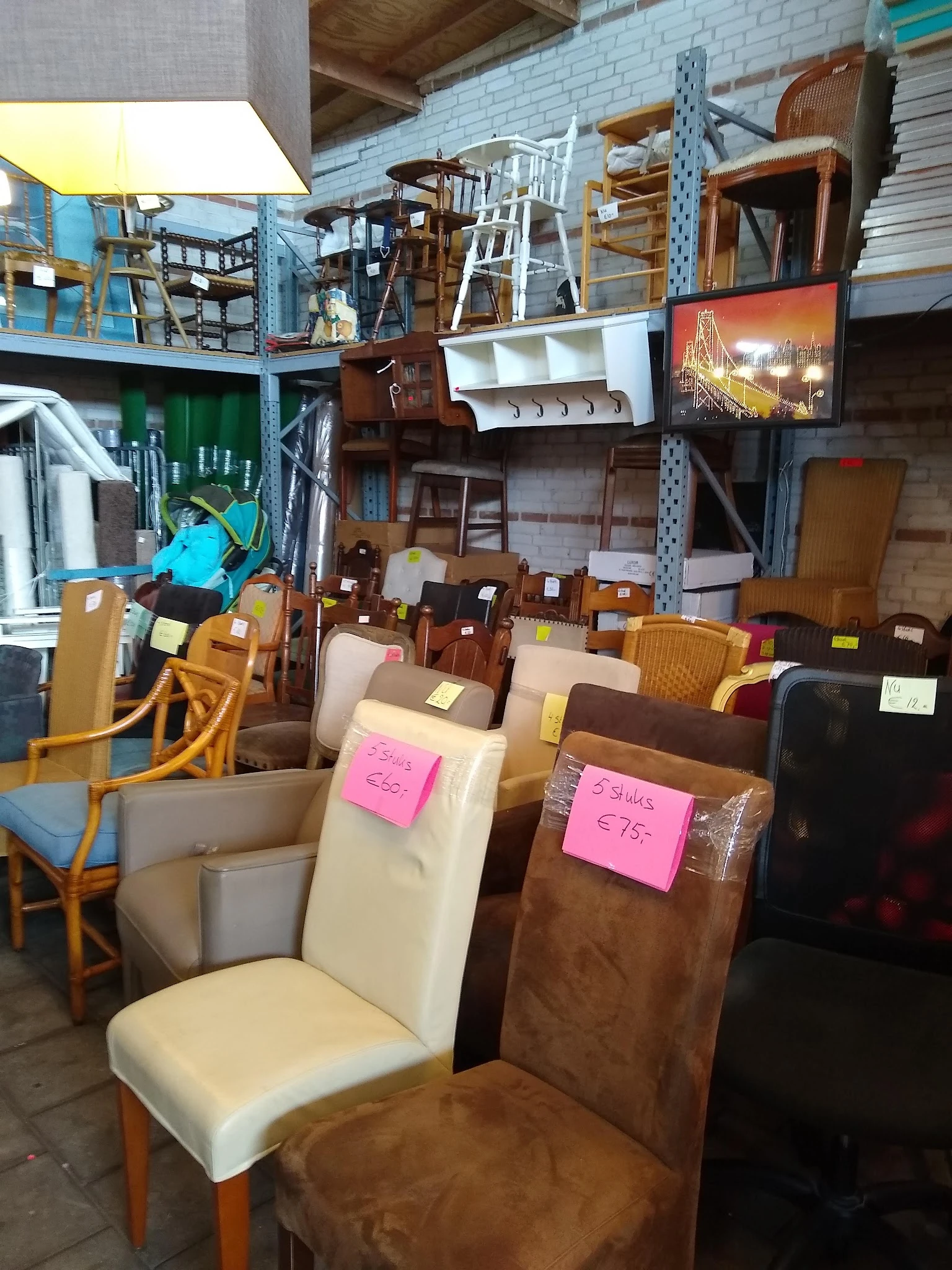 Eetkamerstoelen en zetels met prijsstickers op een rij in een kringloopwinkel
