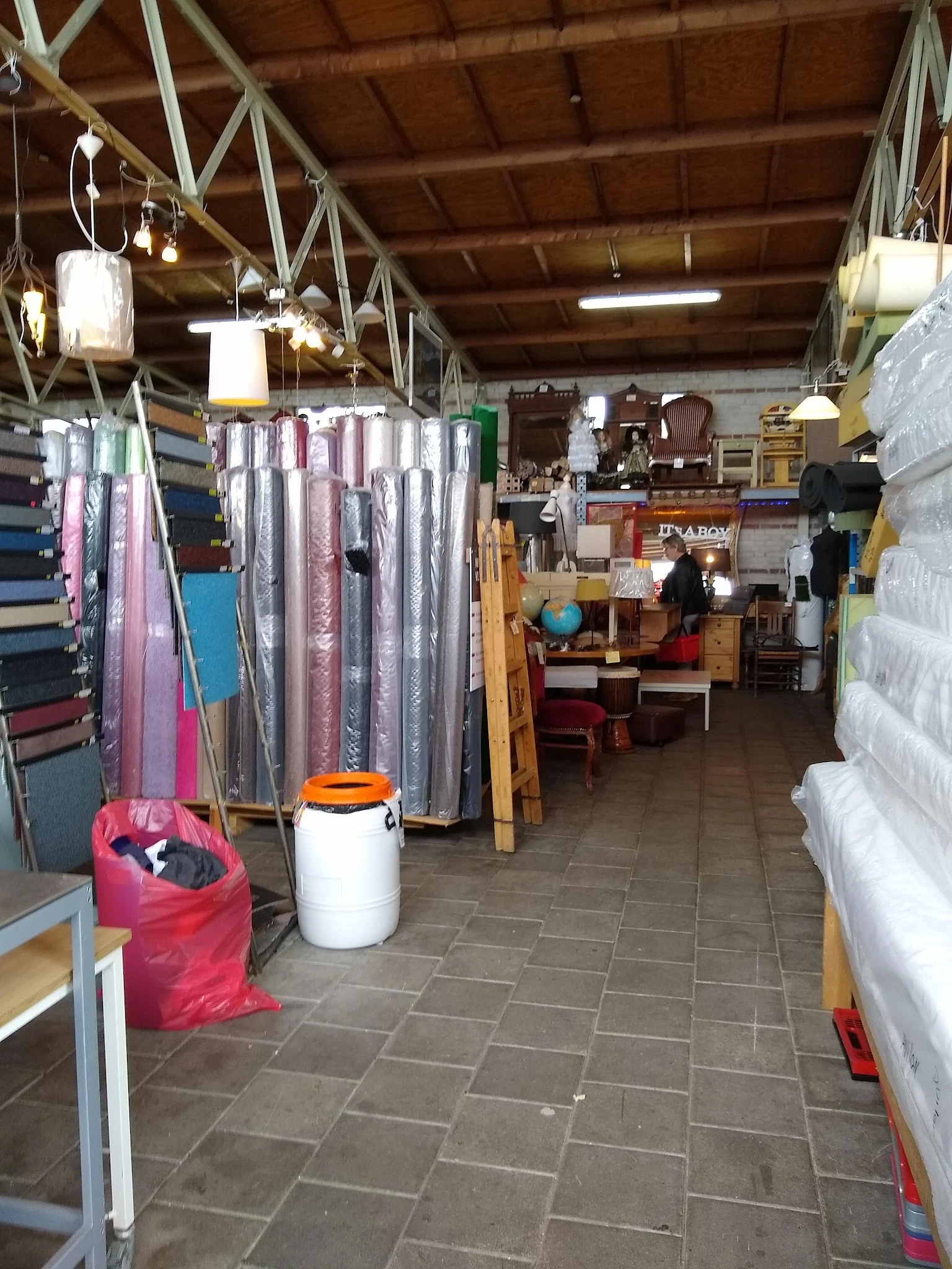 Winkelinterieur met textielen op hangers, stellingen met spullen en een roze afvalbak
