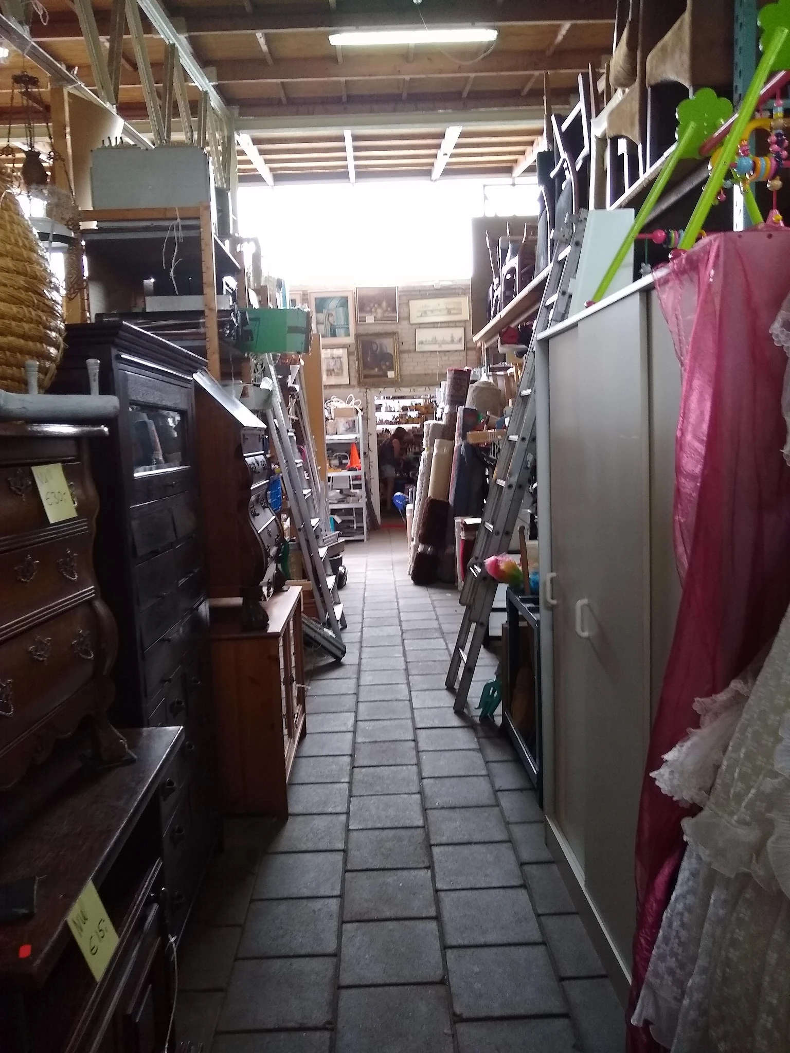 Gangpad tussen stellingen met meubels, textiel en diverse tweedehands artikelen in kringloopwinkel
