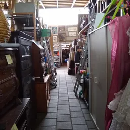 Gangpad tussen stellingen met meubels, textiel en diverse tweedehands artikelen in kringloopwinkel