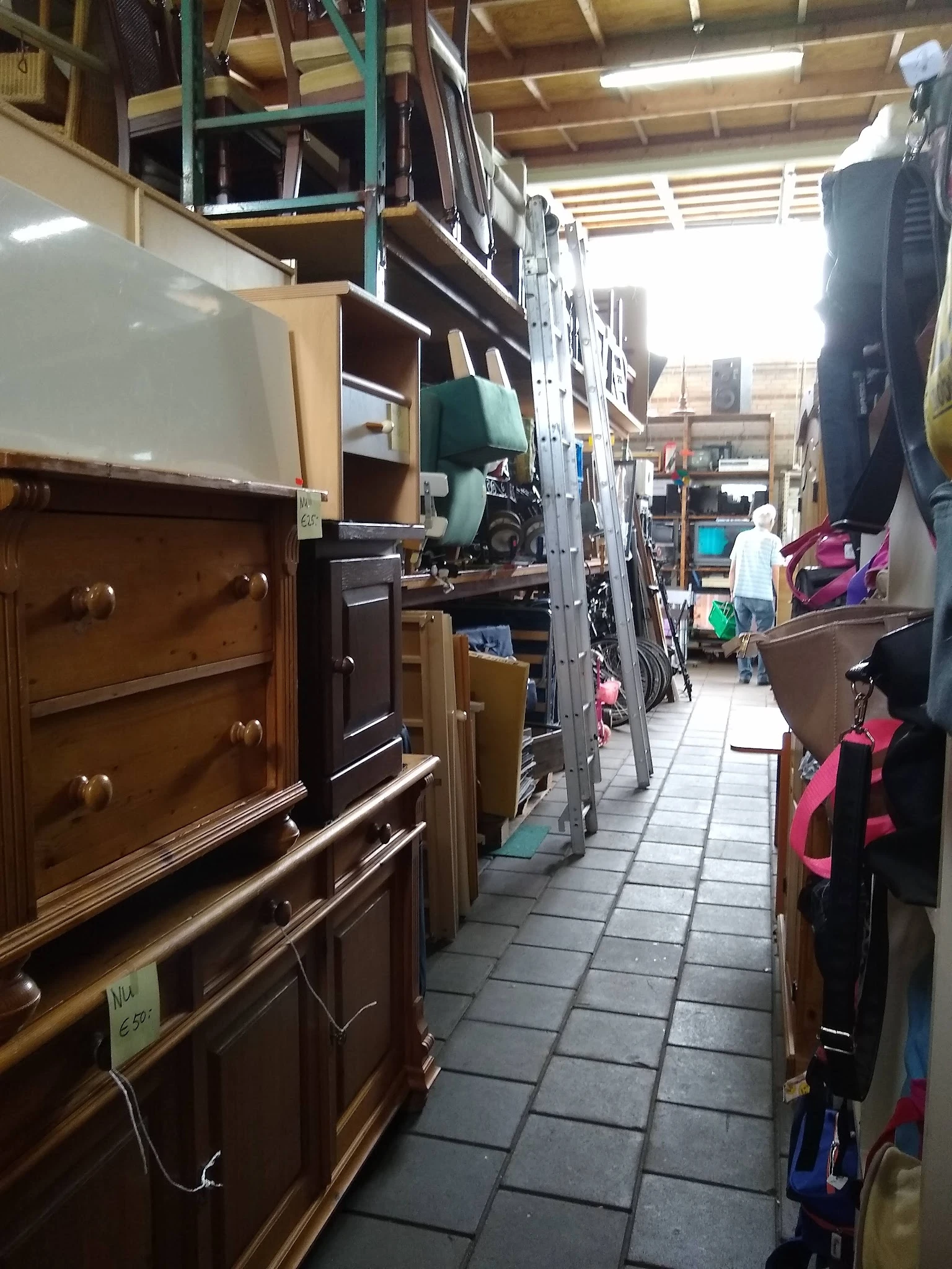 Smalle gangpad tussen meubels en kledingrekken in kringloopwinkel