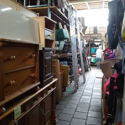 Smalle gangpad tussen meubels en kledingrekken in kringloopwinkel