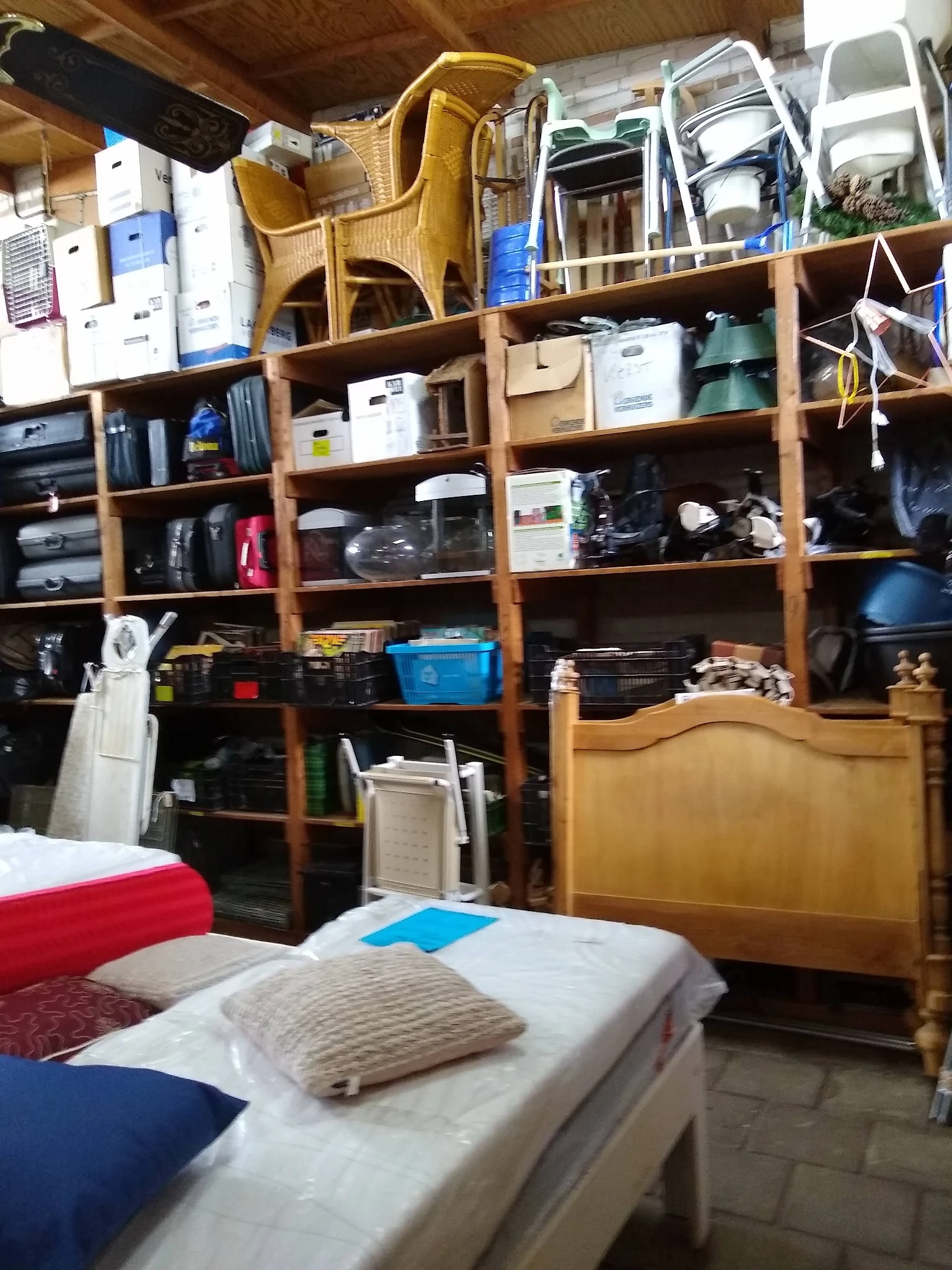Houten stellingkast gevuld met diverse huishoudelijke artikelen en spullen in een kringloopwinkel