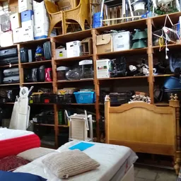 Houten stellingkast gevuld met diverse huishoudelijke artikelen en spullen in een kringloopwinkel