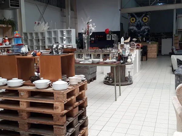 Ruime winkelruimte met verschillende afdelingen, witte tegelvloer, houten meubels en diverse huishoudartikelen en decoraties