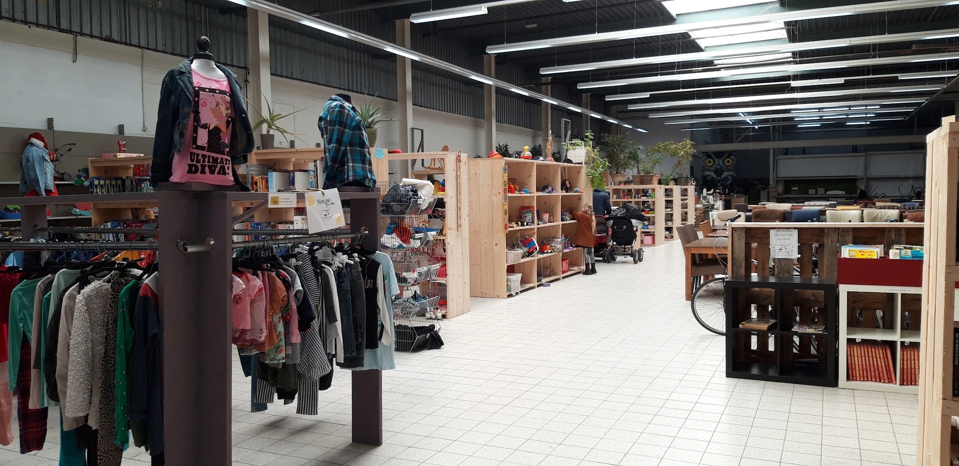 Winkelinterieur met houten stellingen, kleding op rekken, huishoudartikelen en diverse tweedehands spullen