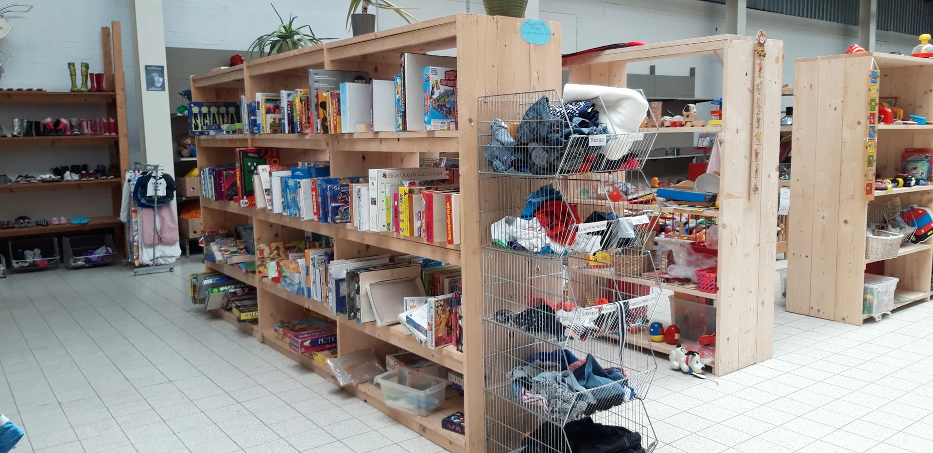 Houten kasten met boeken en speelgoed, metalen stellingen met speelgoedkisten in kringloopwinkel