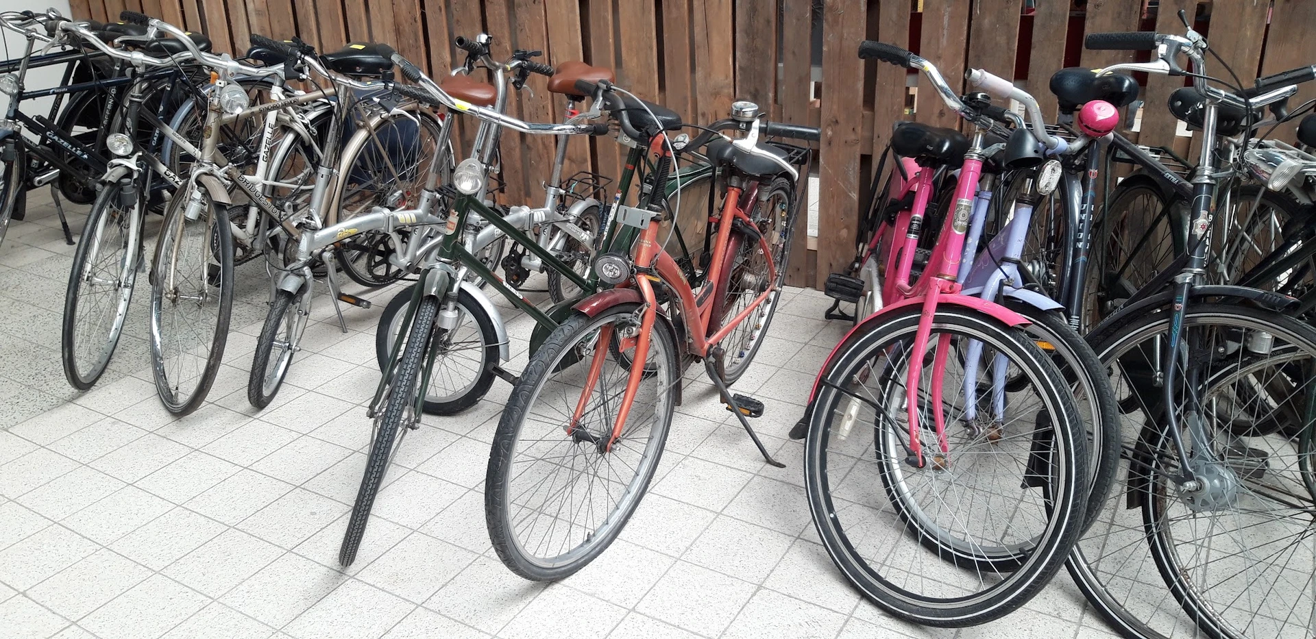Verschillende tweedehands fietsen in verschillende kleuren, opgesteld in een binnentuin of parkeerruimte
