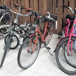 Verschillende tweedehands fietsen in verschillende kleuren, opgesteld in een binnentuin of parkeerruimte