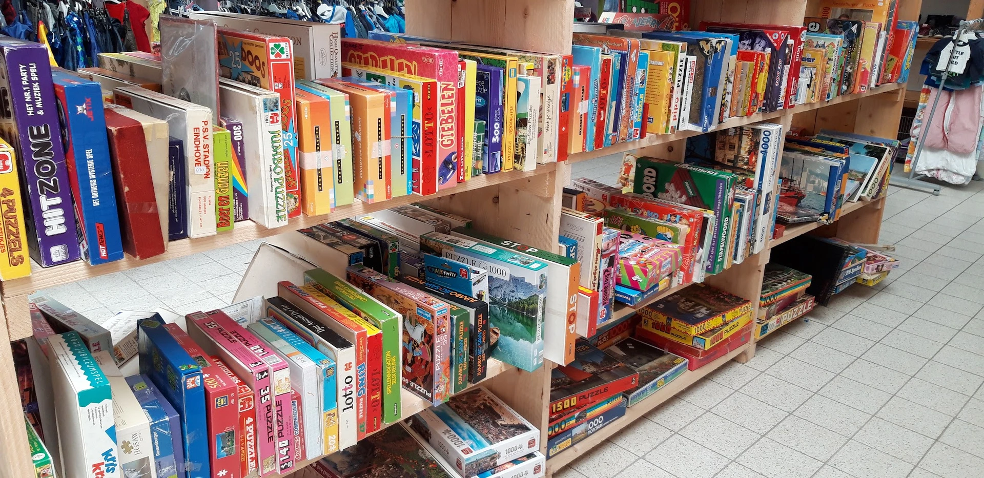 Houten stellingen met grote verzameling tweede hands bordspellen en puzzels, netjes uitgestald in dozen