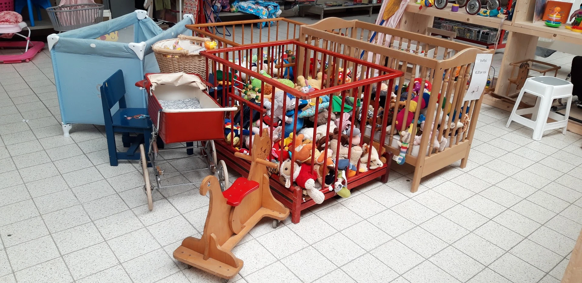 Verschillende babybedhjes en wiegjes in verschillende kleuren (rood, naturel, blauw) met speelgoed en beddengoet.