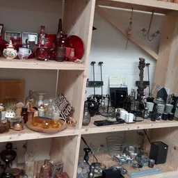 Houten stellingkasten met verzameling tweedehands huishoudartikelen, waaronder rode en zwarte kaarsen, flessen, elektronische