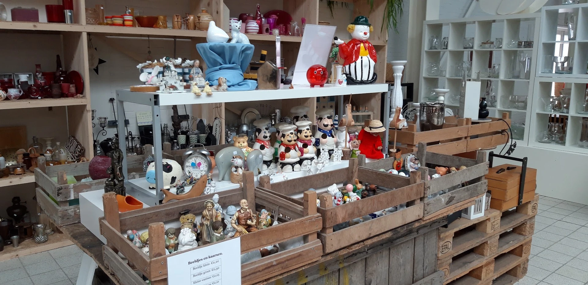 Uitgestalde verzameling decoratieve items en beeldjes in houten bakken en op schappen