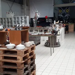 Ruime winkelruimte met diverse uitgestalde spullen op houten pallets en vitrines, witte tegelvloer