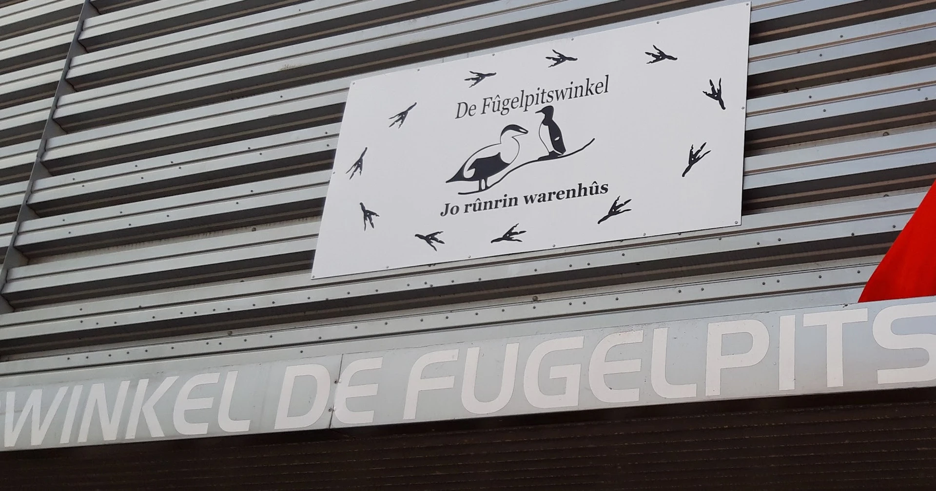 Winkelnaambord 'De Fûgelpitswinkel' met vogelmotief op golfplaten gevel