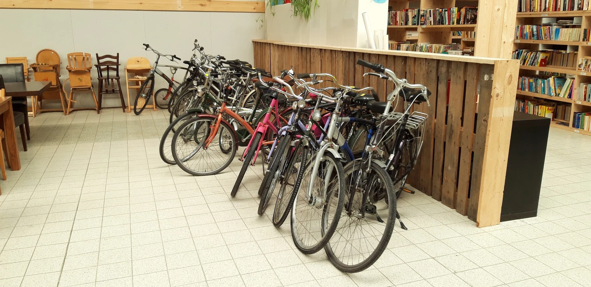 Verzameling tweedehands fietsen in verschillende kleuren tegen houten wand in winkelinterieur