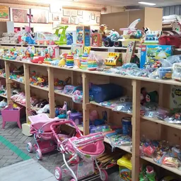 Speelgoedafdeling in kringloopwinkel met houten stellingen vol poppen, speelgoed en kinderspullen, roze poppenwagens op de vl