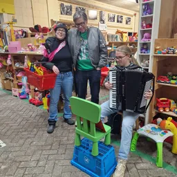 Groep kinderen en volwassenen met speelgoed in een kringloopwinkel, waaronder een accordeon