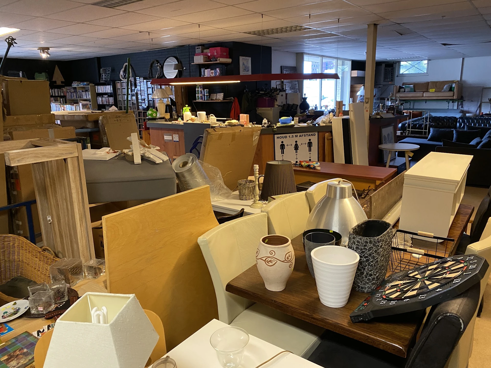 Winkelvloer met tafels, stoelen en diverse huishoudelijke spullen in een kringloopwinkel