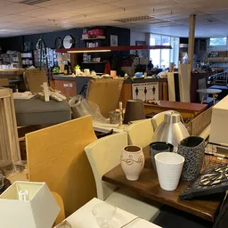 Winkelvloer met tafels, stoelen en diverse huishoudelijke spullen in een kringloopwinkel