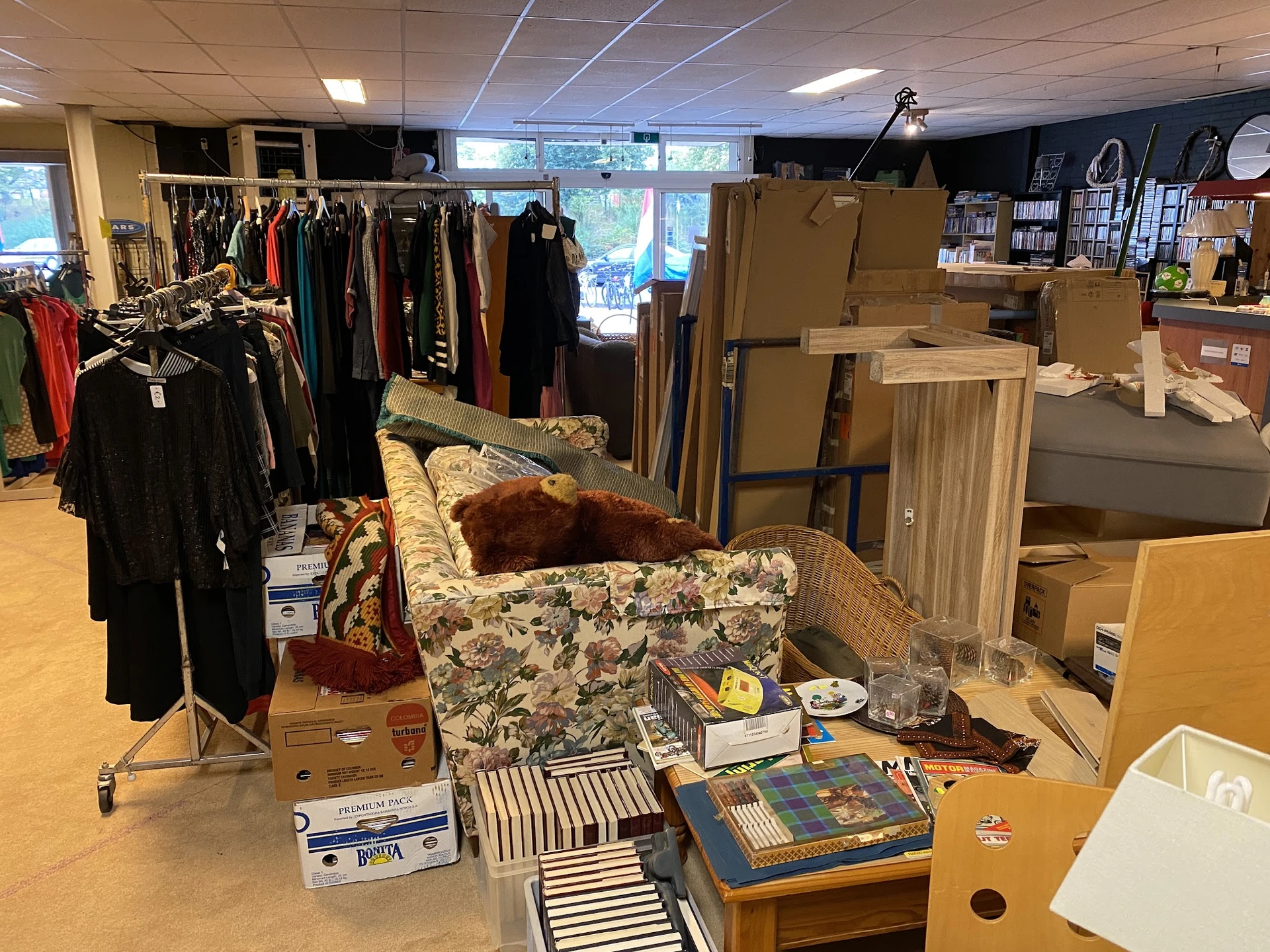 Winkelvloer met uitgepakte dozen, meubels, kledingrekken en diversen tweedehands spullen