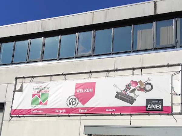 Gevel van kringloopwinkel met welkomsbanner en logo's, grote ramen op eerste verdieping