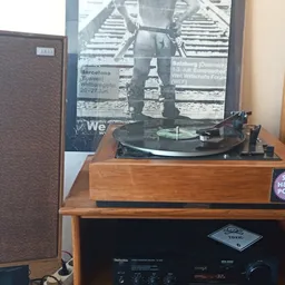 Vintage platenspeler in houten kast op een houten tafel, met versterker eronder en poster op de muur