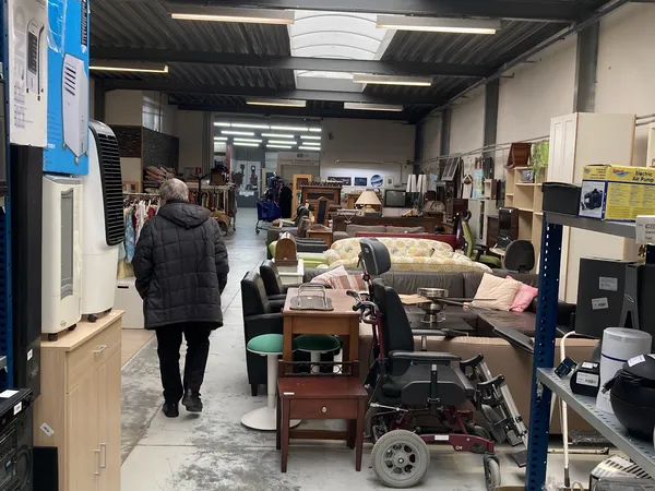 Winkelvloer van kringloopwinkel met meubels, tafels, stoelen en diverse spullen uitgestald onder fluorescente verlichting