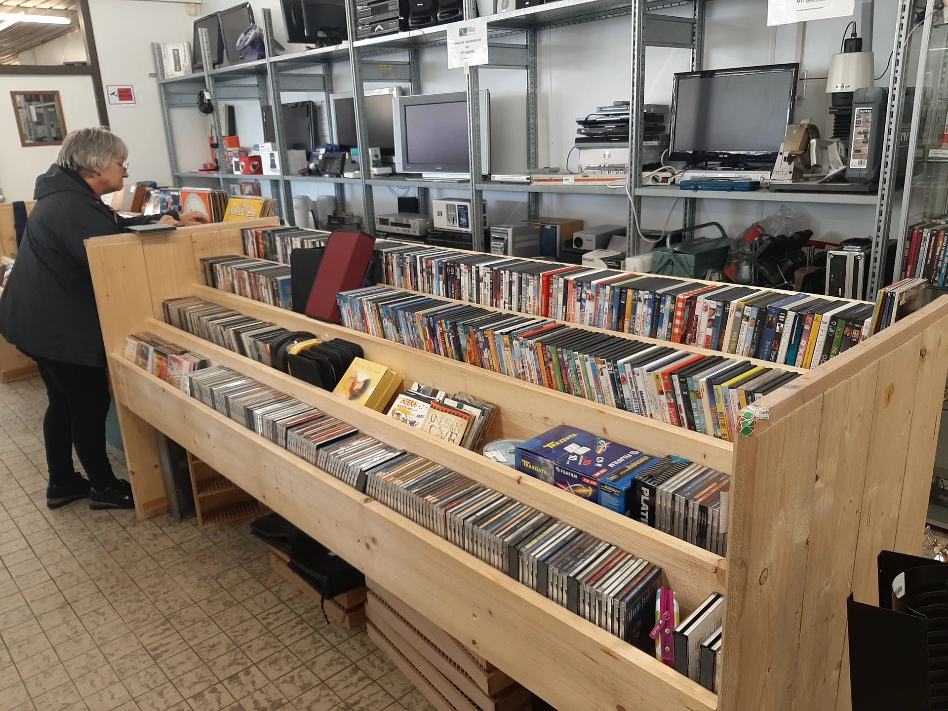 Houten displaykasten met grote collectie cd's en dvd's uitgestald, met een bezoeker in het achtergrond