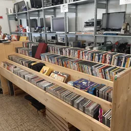 Houten displaykasten met grote collectie cd's en dvd's uitgestald, met een bezoeker in het achtergrond