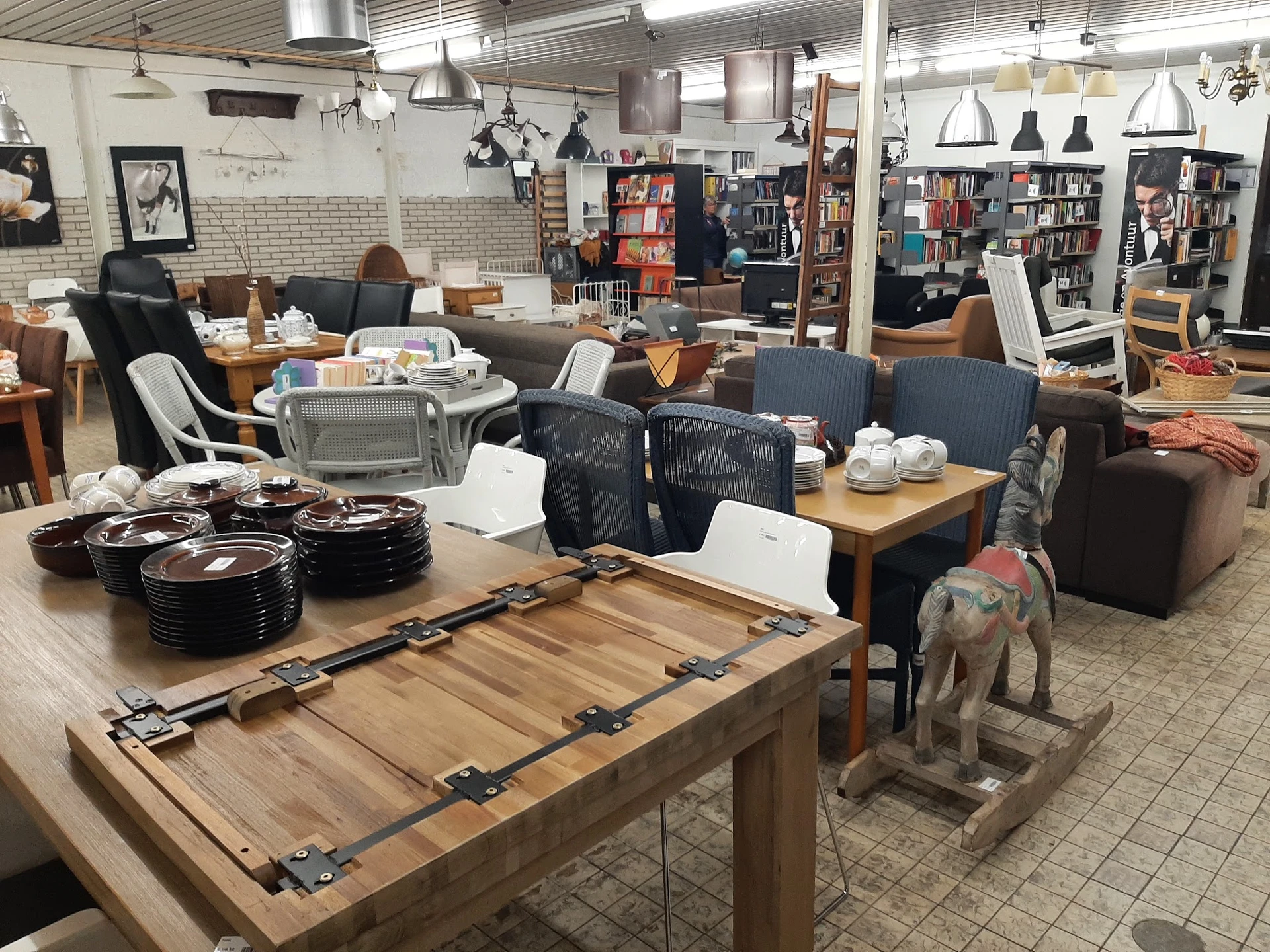 Winkelvloer met houten tafels, zithoeken met zwarte stoelen, boekenkasten en diversen huishoudelijke spullen uitgestald