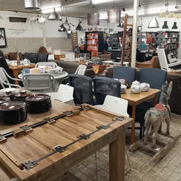 Winkelvloer met houten tafels, zithoeken met zwarte stoelen, boekenkasten en diversen huishoudelijke spullen uitgestald