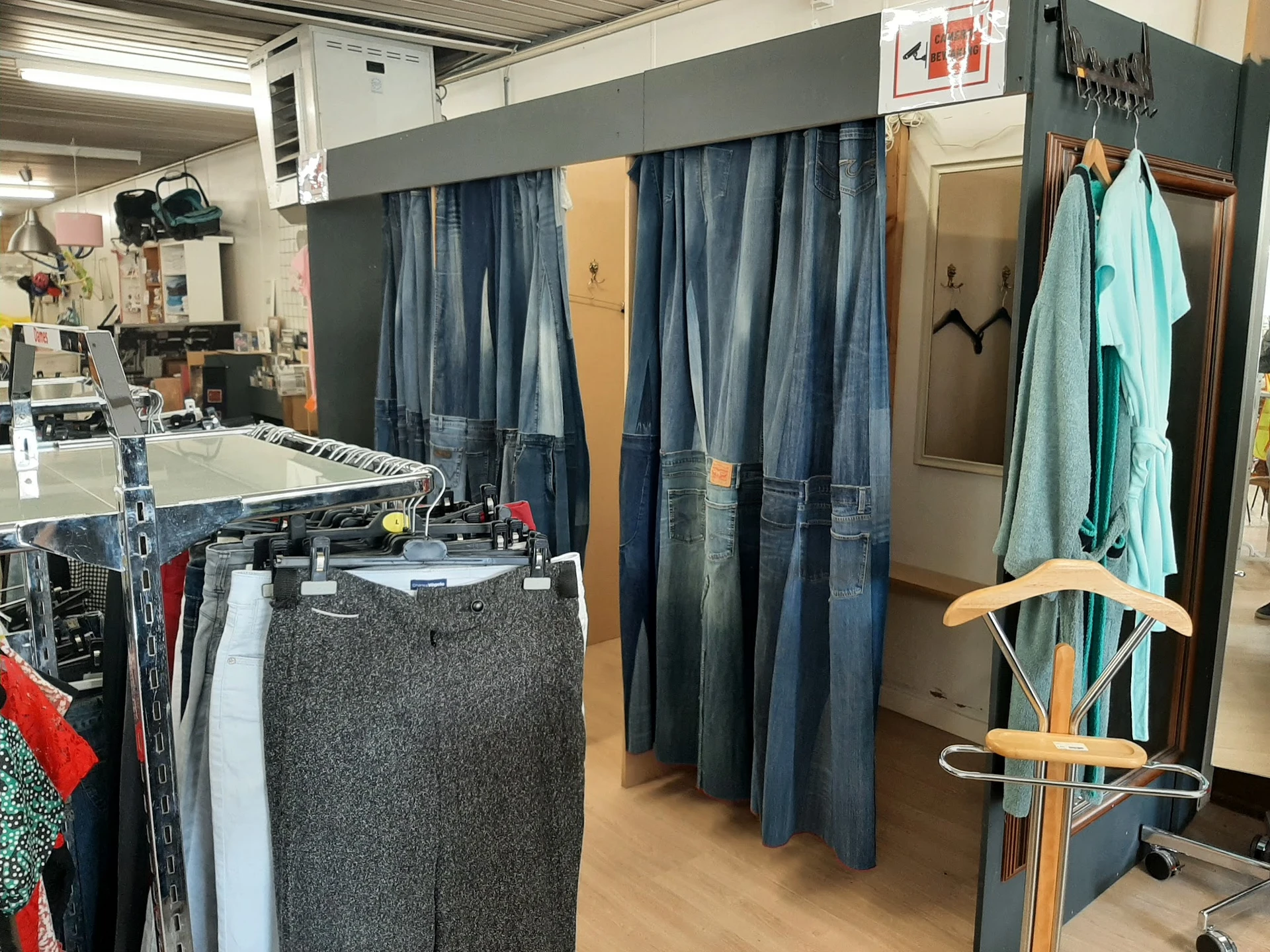 Winkelvloer met kledingrekken, stellingen met tweedehands kleding en paskamers met blauwe gordijnen
