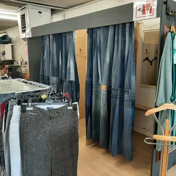 Winkelvloer met kledingrekken, stellingen met tweedehands kleding en paskamers met blauwe gordijnen