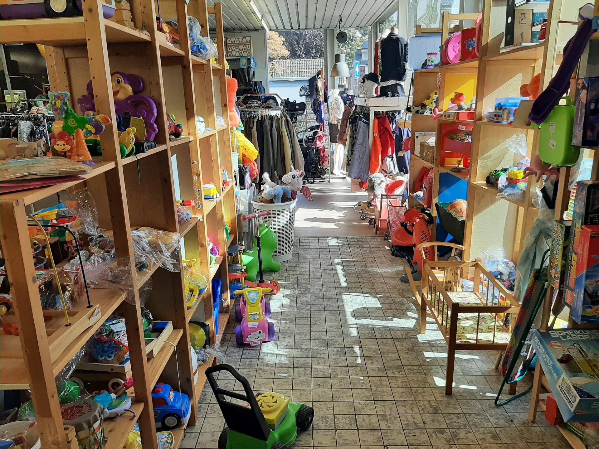 Winkelgang met houten stellingen vol speelgoed, kleding en huishoudartikelen in een kringloopwinkel