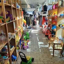 Winkelgang met houten stellingen vol speelgoed, kleding en huishoudartikelen in een kringloopwinkel