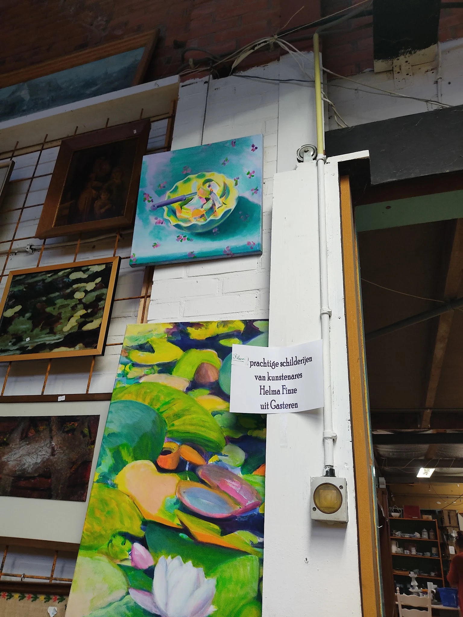 Kunstwerken en schilderijen aan de muur, waaronder gele en groene doeken met abstracte motieven