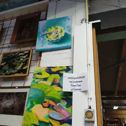 Kunstwerken en schilderijen aan de muur, waaronder gele en groene doeken met abstracte motieven