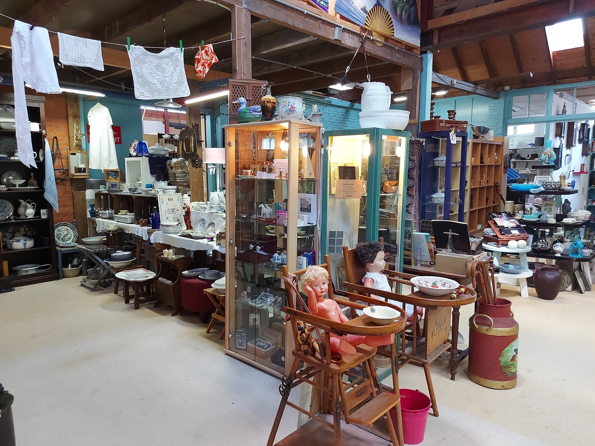 Winkelvloer met meubels, vitrines, tafels en stoelen uitgestald; witte doeken hangen aan het plafond