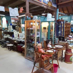 Winkelvloer met meubels, vitrines, tafels en stoelen uitgestald; witte doeken hangen aan het plafond